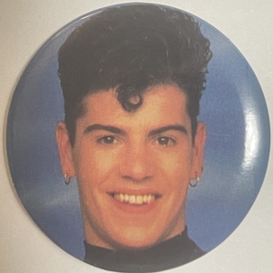 Front of the round New Kids on the Block pinback, a close-up color photo of Jordan Knight smiling in a black turtleneck against a blue studio backdrop.