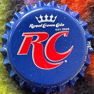 May include: Blue and red Royal Crown Cola bottle cap with the logo "RC" and the text "Royal Crown Cola Est. 1905".