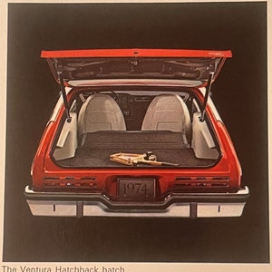 May include: A red 1974 Ventura Hatchback with the boot open, showing the interior. The car has white seats and a black cargo area. A fishing rod is visible in the cargo area. The text "1974" is on the number plate.
