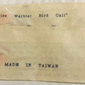 May include: A white paper envelope with the text "Swiss Warbler Bird Call" and "MADE IN TAIWAN" printed on it.