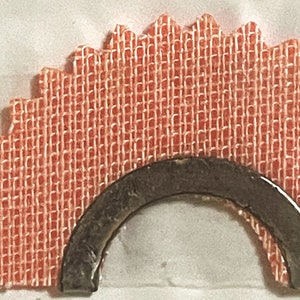 May include: A close-up of a red fabric starburst with a metal arch attached to the center. The fabric has a woven texture.