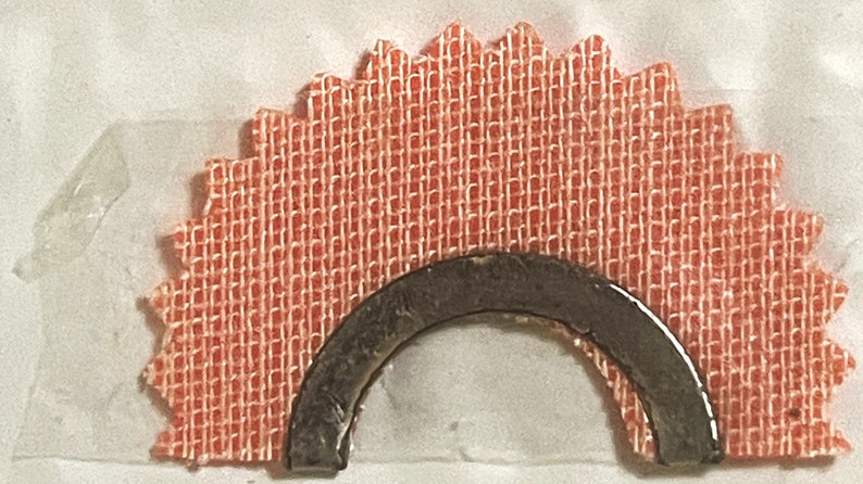 May include: A close-up of a red fabric starburst with a metal arch attached to the center. The fabric has a woven texture.