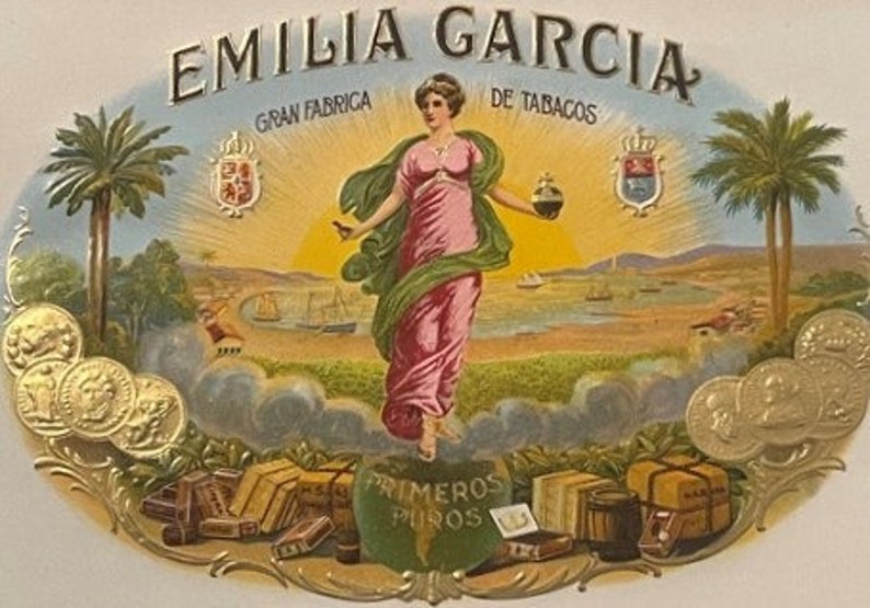 Puede incluir: Una etiqueta de caja de cigarros vintage con una mujer con un vestido rosa y verde de pie en un paisaje con palmeras. La etiqueta dice "Emilia Garcia Gran Fabrica de Tabacos Primeros Puros".