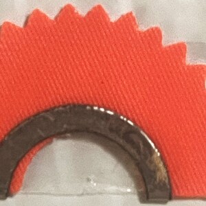 May include: A bright orange fabric target with a silver metal ring in the center. The target is shaped like a half circle with a scalloped edge.