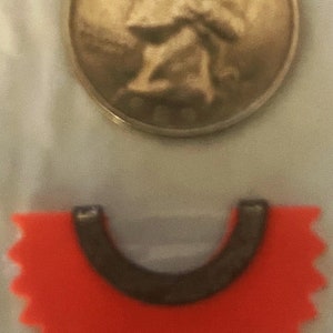 May include: A red, star-shaped, plastic token with a black, U-shaped cutout in the center. The token is similar to a game piece.