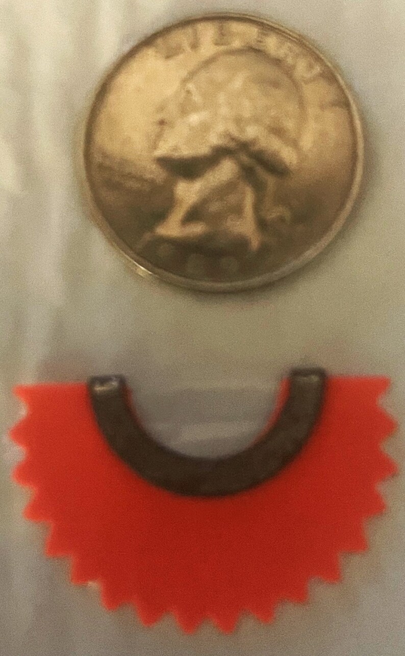 May include: A red, star-shaped, plastic token with a black, U-shaped cutout in the center. The token is similar to a game piece.