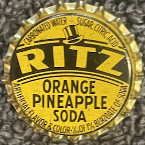 May include: Yellow bottle cap with black text that reads "CARBONATED WATER SUGAR, CITRIC ACID" and "RITZ ORANGE PINEAPPLE SODA ARTIFICIAL FLAVOR & COLOR - % OF 1% BENZOATE OF SODA".