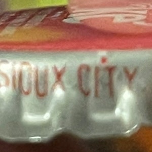 Op de afbeelding: Close-up van een zilveren dop met rode letters die "COMPANY SIOUX CITY IOWA 51102" lezen.