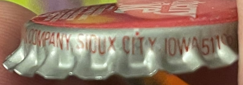 Op de afbeelding: Close-up van een zilveren dop met rode letters die "COMPANY SIOUX CITY IOWA 51102" lezen.