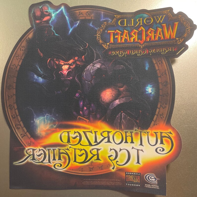 May include: A World of Warcraft Trading Card Game mousepad featuring a dark-skinned character with horns and a lightning bolt in their hand. The background is a dark, circular design with the words "World of Warcraft" and "Trading Card Game" in a gold and black font.