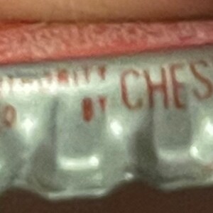 Op de afbeelding: Een zilveren flessen dop met een rood en wit etiket. Het etiket vermeldt "Chesterfield" en "Registered Trademark" met een klein logo.