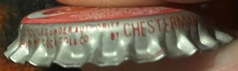 Op de afbeelding: Een zilveren flessen dop met een rood en wit etiket. Het etiket vermeldt "Chesterfield" en "Registered Trademark" met een klein logo.