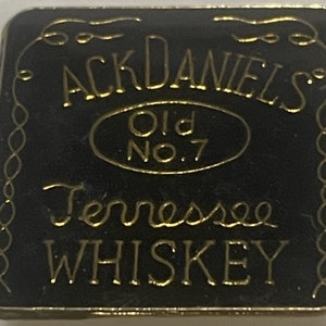 May include: Black square pin with gold lettering that reads "Jack Daniel's Old No. 7 Tennessee Whiskey".