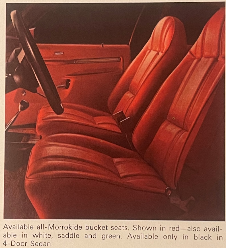 May include: A vintage car interior with red bucket seats. The seats are made of a textured material and have a classic design. A black steering wheel and part of the dashboard are visible. The image is from an advertisement.