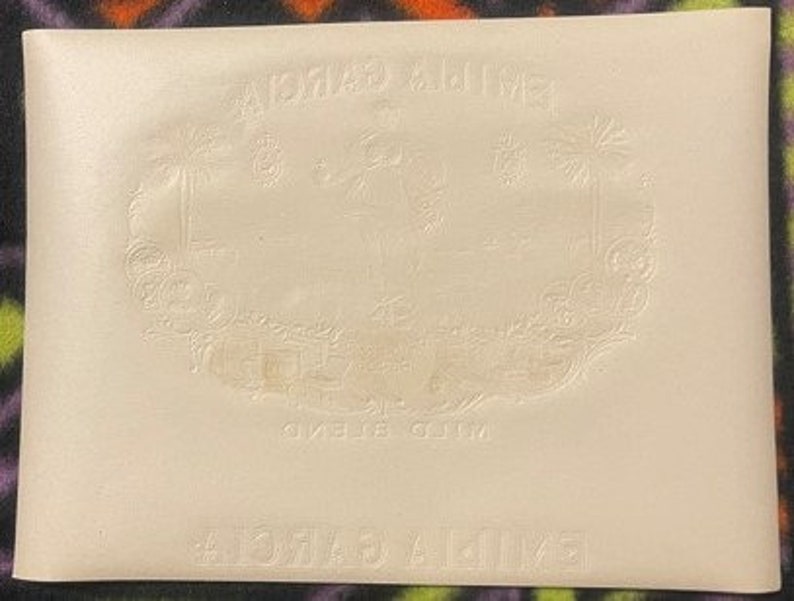 Puede incluir: Una bolsa de cuero blanco con las palabras "A.C.M.A.S. & MILLER" en relieve en la parte delantera. La bolsa tiene un dise&ntilde;o decorativo de palmeras y una ciudad.