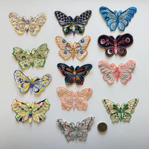 Puede incluir: Una colección de parches de mariposas bordadas en varios colores y diseños. Los parches presentan detalles intrincados y una variedad de colores, incluyendo azul, rosa, verde y amarillo. Los parches están dispuestos sobre una superficie blanca.
