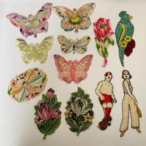 Puede incluir: Una colección de parches bordados coloridos con mariposas, flores, un pájaro y figuras con ropa vintage. Los parches muestran detalles intrincados y una variedad de colores, incluyendo rosa, verde y amarillo.