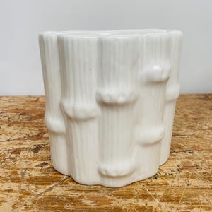Op de afbeelding: Witte keramische plantenbak in de vorm van bamboestokken. De plantenbak is een eenvoudig, modern ontwerp.