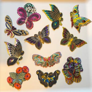 May include: A selection of embroidered butterfly patches in diverse colours and designs. The patches feature intricate details with gold, purple, pink, and blue thread. These decorative patches are ideal for adding a unique touch to clothing or accessories.