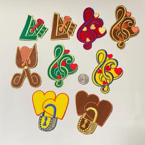 Op de afbeelding: Tien geborduurde strijkpatches met verschillende ontwerpen, waaronder harten, muzieknoten en het woord "LOVE". De patches zijn in verschillende kleuren, waaronder rood, groen, geel, bruin en blauw.