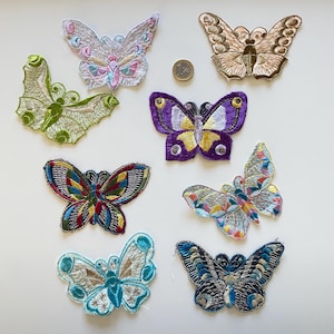 Puede incluir: Colección de ocho parches de mariposas bordadas en varios colores y diseños. Los parches presentan costuras detalladas y una variedad de colores, incluyendo verde, morado, azul y dorado. Se incluye una moneda como referencia de tamaño. Estos parches son ideales para añadir un toque decorativo a la ropa o accesorios.