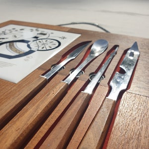 Op de afbeelding: Een set van vijf zilveren bestekdelen met houten handvatten, gepresenteerd op een houten dienblad. Het bestek omvat een lepel, een mes en drie vorken.