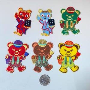 Op de afbeelding: Zes geborduurde strijk-op patches met cartoon beren in verschillende kleuren en outfits. De beren dragen hoeden, overalls en dragen emmers.