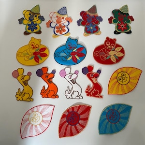 May include: A selection of colourful embroidered patches featuring whimsical bear and mouse designs. The patches include various colours, such as yellow, blue, red, and orange, with floral and leaf accents. Some patches have hats.