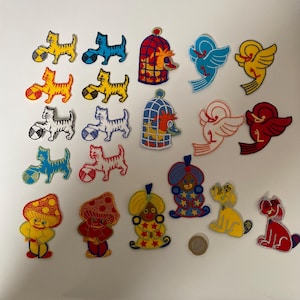 Puede incluir: Una colección de parches bordados coloridos con varios diseños. Se incluyen gatos con pelotas, pájaros, jaulas, setas, un genio, un perro y una moneda. Los parches son en tonos de amarillo, rojo, azul, blanco y naranja.