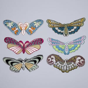 Op de afbeelding: Zes geborduurde vlinder- en motpatches met diverse kleurenpaletten, waaronder blauw, oranje, roze, groen, geel en bruin. Elke patch toont ingewikkeld draadwerk met verschillende vleugelpatronen, vormen en decoratieve texturen.