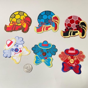 Puede incluir: Parches bordados con balones de fútbol y caras de payaso. Los parches de balón de fútbol son amarillos, azules y rojos, combinados con zapatos a juego. Los parches de payaso son blancos, azules y rojos, cada uno con un sombrero y una pajarita.