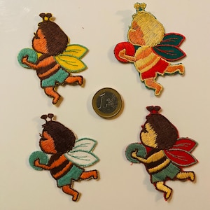 May include: Four embroidered bee patches in various colours, including brown, orange, yellow, green, and red. Each patch features a cartoon bee holding a ball. A Euro coin is next to the patches.