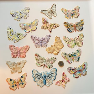 Pode incluir: Uma coleção de patches de borboletas bordadas em várias cores e designs. Os patches apresentam detalhes intrincados e uma variedade de cores, incluindo rosa, amarelo, azul e verde. Uma moeda está incluída para referência de tamanho.