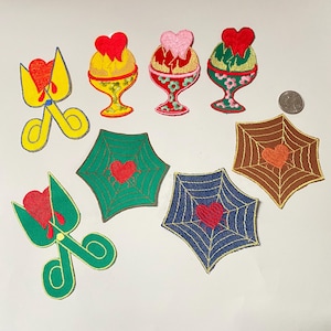 May include: Nine embroidered iron-on patches featuring a heart with a drop of blood and various designs, including scissors, spiderwebs, and ice cream cones.