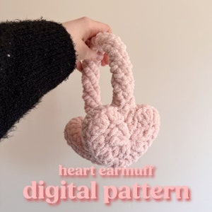 May include: Pink heart-shaped earmuffs made of yarn. The earmuffs are held by a hand and the text "heart earmuff digital pattern" is below the earmuffs.
