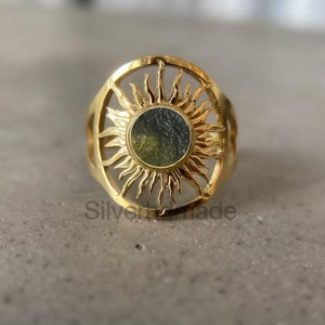 May include: Gold ring with a sun design and a green and black stone in the center.