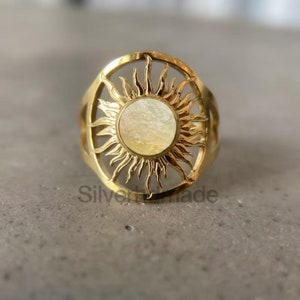 Puede incluir: Anillo de oro con un diseño de sol y un centro de nácar blanco.