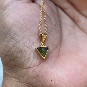 Pode incluir: Um colar de corrente de ouro com um pingente triangular com uma gema verde.