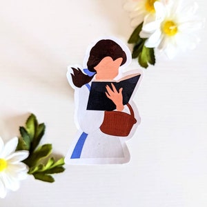May include: A sticker featuring a cartoon illustration of a woman with brown hair reading a book. She is wearing a white dress with a blue sash and a brown bag.