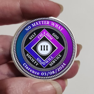 Peut inclure: Une pièce de monnaie argentée avec un motif bleu, violet et noir. La pièce porte les mots "NO MATTER WHAT", "SELF", "FREEDOM", "GOD", "SOCIETY", "GOOD WILL SERVICE". Le centre présente un losange avec le chiffre romain "III". La pièce porte également le nom "Clarence" et la date "03/08/2024".