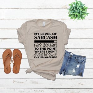 May include: A beige t-shirt with black text that reads "MY LEVEL OF SARCASM has gotten TO THE POINT WHERE I DON'T even know if I'M KIDDING OR NOT". The text is displayed above a black progress bar that is almost full.