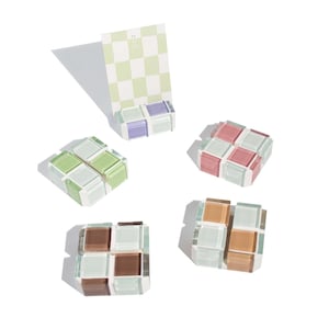 May include: Four small glass cube-shaped paperweights in different colors: green, pink, purple, and brown. Each cube is made of small glass squares.