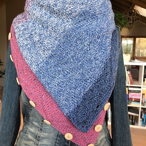 Op de afbeelding: Een gebreide sjaal met een blauw en roze ombre-ontwerp. De sjaal heeft houten knopen aan de randen.