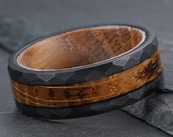 Puede incluir: Un anillo negro y marrón con una banda negra texturizada y una incrustación de madera. El anillo está hecho de carburo de tungsteno y madera.