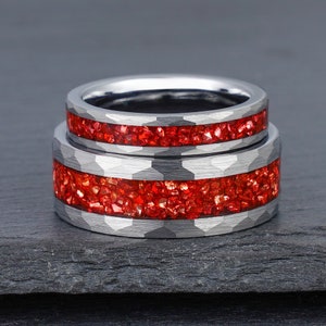 May include: Two silver-toned rings with a hammered finish and a central inlay of crushed red stone. The rings feature a metallic band with a textured, faceted surface and a vibrant, sparkling red inlay that runs horizontally around the centre.