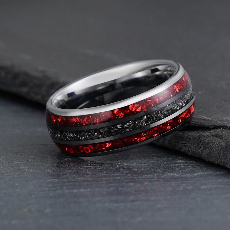 Peut inclure: Une bague en m&eacute;tal argent&eacute; dot&eacute;e d'une bande polie avec trois canaux incrust&eacute;s distincts. Les canaux ext&eacute;rieurs contiennent un mat&eacute;riau broy&eacute; rouge vif, tandis que le canal central est rempli d'un mat&eacute;riau broy&eacute; noir textur&eacute;.