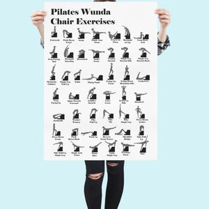 May include: A white poster titled "Pilates Wunda Chair Exercises" featuring black illustrations of various Pilates exercises. The poster is held by a person against a light blue background. The exercises are labeled with text.