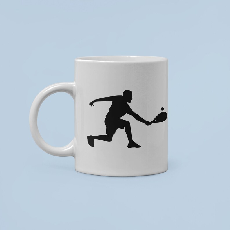 May include: White ceramic mug with a black silhouette of a person playing paddleball. The person is in mid-swing, holding a paddle and a ball is in the air.