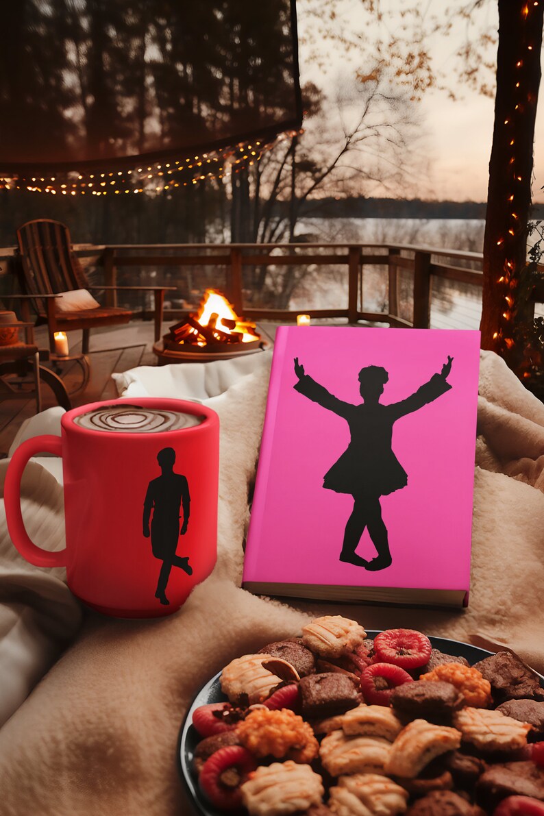 May include: A red mug with a silhouette of a person dancing on it, a pink book with a silhouette of a person dancing on the cover, and a plate of cookies on a brown surface.