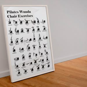 May include: A framed Pilates Wunda Chair Exercises poster. The white poster features black silhouettes demonstrating various exercises. The poster is in a white frame and leans against a white wall and a wooden floor.